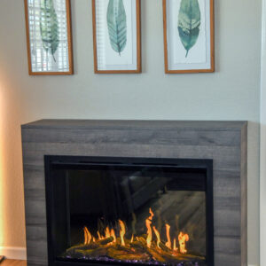 picture of an electric fireplace in a wood cabinet under 3 framed pitures of leaves