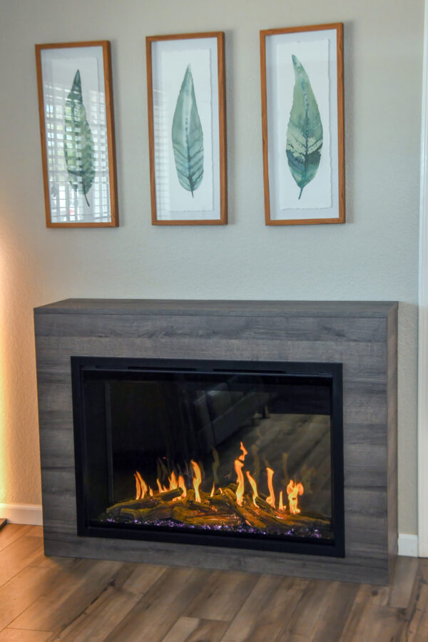 picture of an electric fireplace in a wood cabinet under 3 framed pitures of leaves